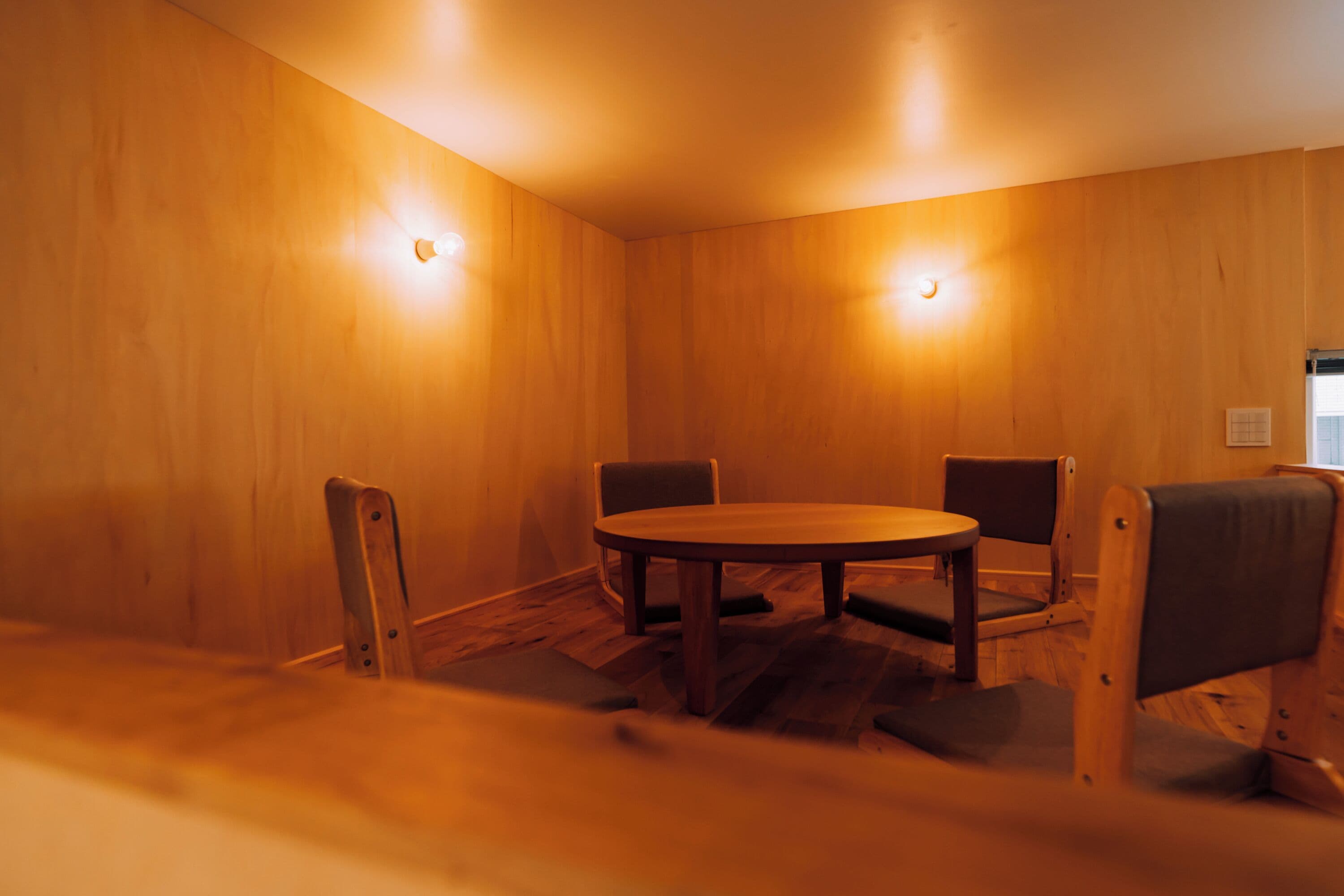 Een vergaderzaal met een houten tafel en vier stoelen, houten wanden en twee wandlampen.