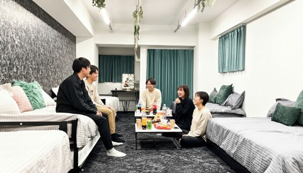 Ein modernes Hotelzimmer mit einer Couch, zwei Einzelbetten, einem kleinen Tisch mit Snacks und einem Fernseher.