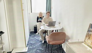 Una habitación con una mesa redonda, una computadora portátil, una silla y una persona usando una tableta.