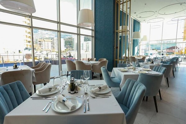 A restaurant with tables set for dining, large windows, and a view of buildings. - Status M Apartments WOW (Budva)
