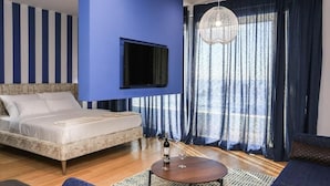 Ein Schlafzimmer mit einem Bett, einem an der Wand montierten Fernseher, einer Kristallleuchtre und Blick ins Freie durch große Fenster.