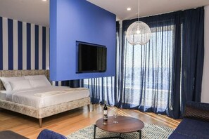 A bedroom with a bed, a television mounted on the wall, a chandelier, and a view of the outdoors through large windows. - Status M Apartments WOW (Budva)