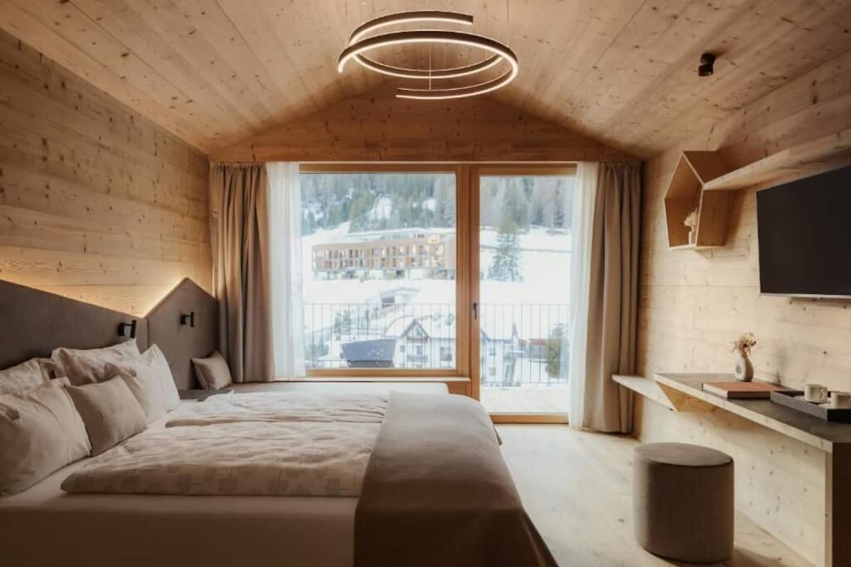 Un dormitorio de cabaña de madera con una cama, un televisor montado en la pared y vistas a un paisaje nevado.