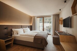 A modern bedroom with a large bed, a desk, a chair, and a TV. - Hotel La Müda (Badia)
