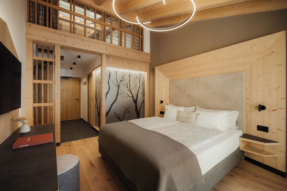 Una habitación de hotel moderna con diseño tipo loft, una cama grande, paredes de madera y un televisor empotrado.