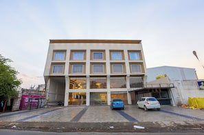 A multi-story building with a central entrance, a blue car parked in front, and a white car parked to the side. - Hotel Nova Platinum Ujjain (Ujjain)