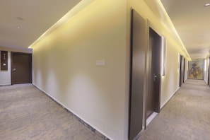 Un pasillo de hotel con puertas, piso alfombrado y pared de color claro.