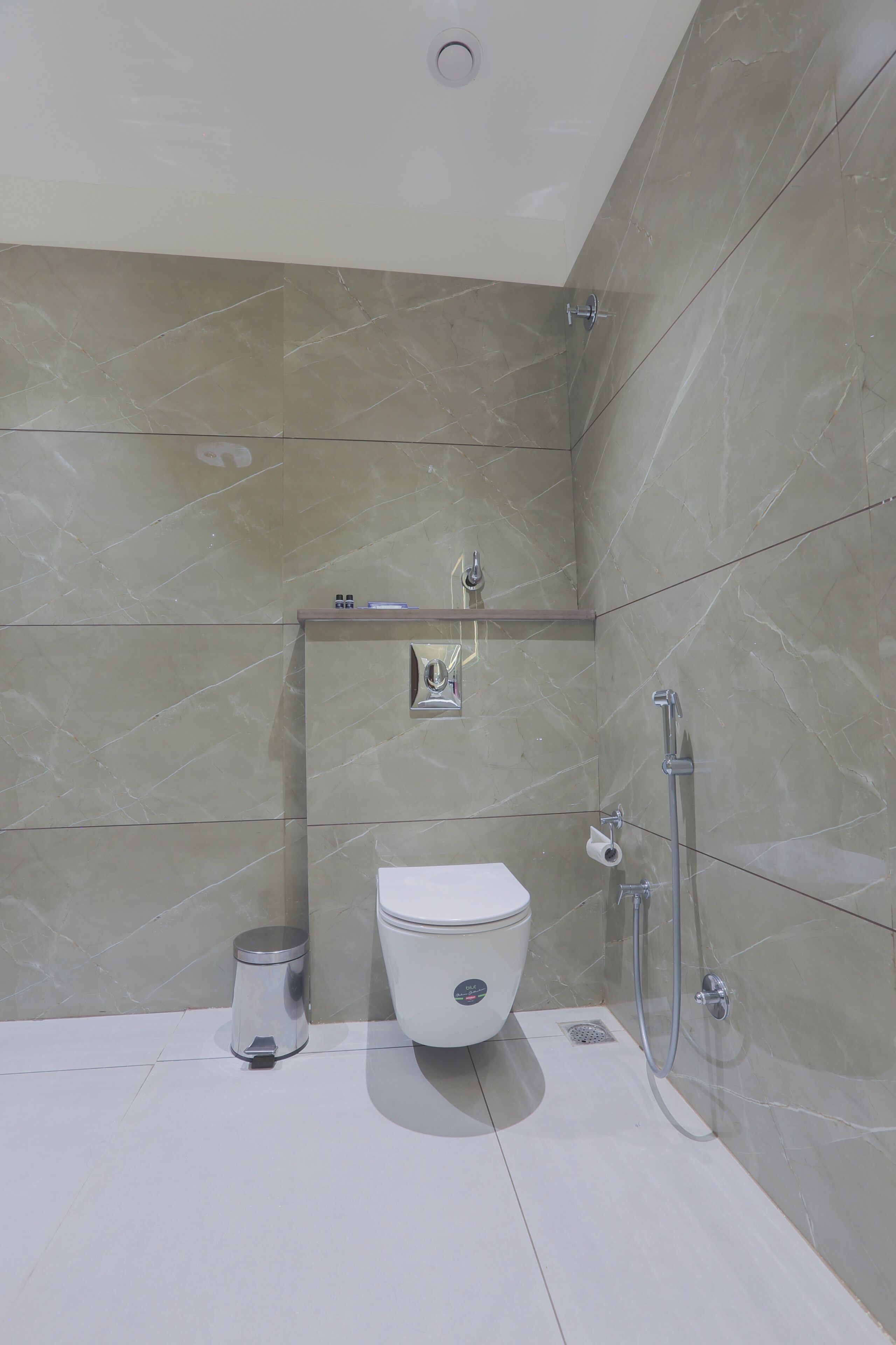 Un bagno moderno con il water, un cestino, una doccia e uno scaffale sopra il water.