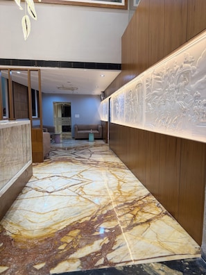 Vestíbulo de hotel con piso de mármol, paneles de madera, mostrador de recepción y una pared con un relieve escultórico.