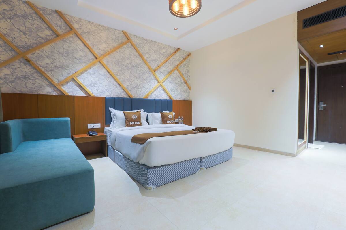 Una habitación de hotel moderna con una cama grande, una mesita de noche, un sillón azul y una pared con diseño de mármol.
