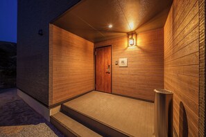Pared exterior de madera con una puerta y un pequeño escalón que conduce a un porche cubierto.