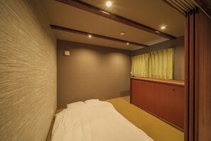 Een hotelkamer met een bed, een houten kledingkast, een raam met gordijnen en inbouwspots.