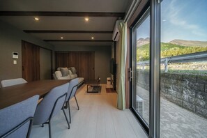 Una habitación moderna con una mesa de comedor de madera, sillas grises, un sofá y un gran ventanal con vistas a la montaña.