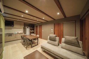 Una cocina moderna con electrodomésticos integrados, una zona de comedor con mesa y sillas de madera, y un sofá con cojines.