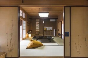 A traditional Japanese room with tatami flooring, a tatami mat table, a yellow cushion, and sliding doors.