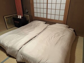 Et værelse med en traditionel japansk shoji-skærm, en seng med hvide sengetøj og et lille bord med en rød genstand på.