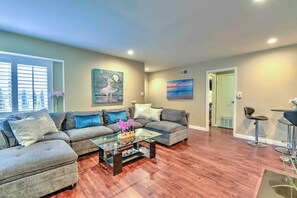 A living room with a sectional sofa, a glass coffee table, and two paintings on the walls.