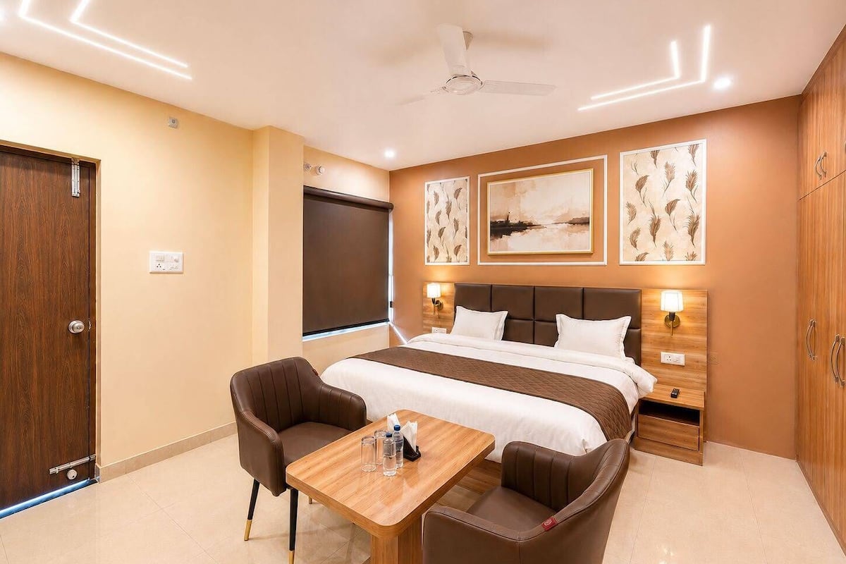 A hotel room with a bed, two bedside tables with lamps, a desk with chairs, a ceiling fan, and artwork on the walls.