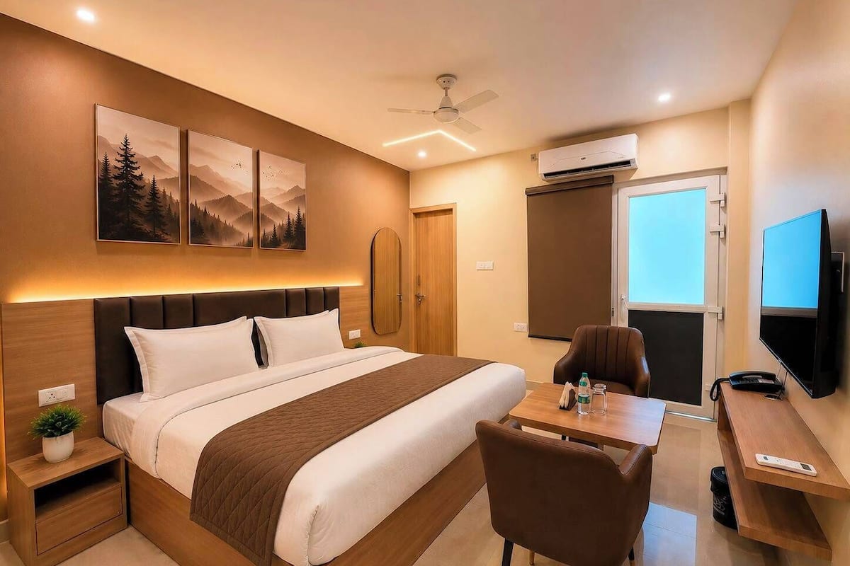A hotel room with a bed, a desk, a chair, a TV, an air conditioning unit, and a ceiling fan.