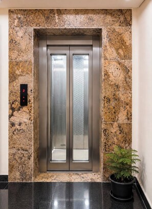 An elevator with a digital display, a potted plant, and a marble wall.
