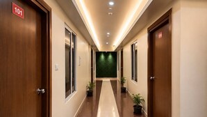 Un pasillo de hotel con puertas de madera, placas de identificación de habitaciones numeradas y plantas en macetas.