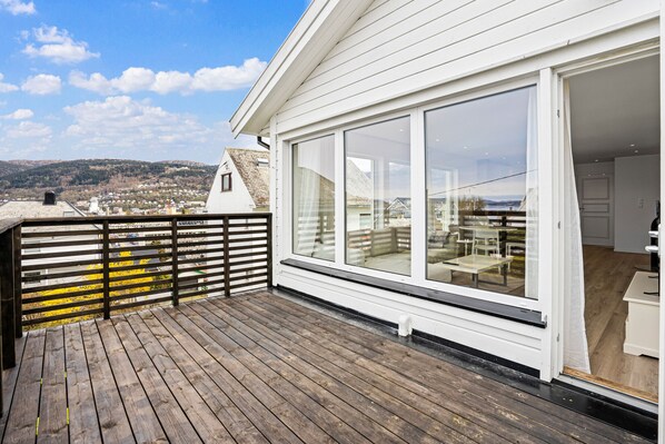 A wooden deck with a glass door leading to a room with a view of a town and hills.