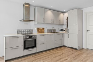A modern kitchen with white cabinetry, a stainless steel range hood, a microwave, and a wooden countertop.