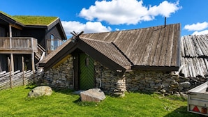 Ein rustikales Steinhaus mit grüner Tür, einer Holzveranda und einem geneigten Dach.