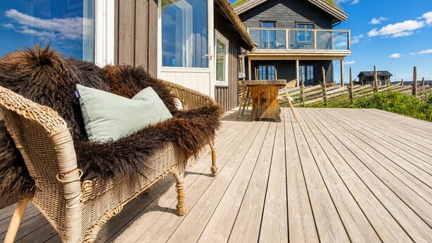 Eine Holzterrasse mit einer Rattansofa und einem kleinen Holztisch.