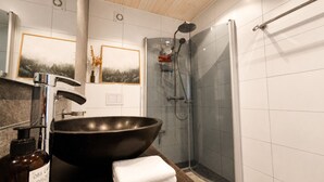 Ein Badezimmer mit einem großen, schwarzen Waschbecken, einer Dusche und einer Holzbeschichtung an der Decke.