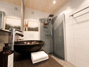 Un baño con un lavamanos negro grande, ducha y techo de madera.