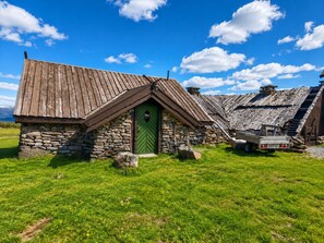 A rustic stone house with a green door, a sloped roof, and a small adjacent shed.