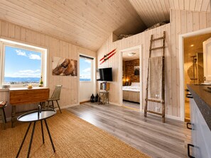A room with wooden walls, a TV, a desk, a chair, a bed, and a view of the outdoors.
