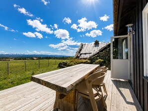 A wooden deck with a table and chairs, a stone wall, and a view of mountains.