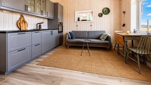 Eine moderne Küche mit grauen Schränken, einer Holzbalkendecke und einem Essbereich mit Tisch und Stühlen.