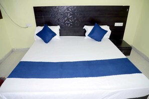 Una cama con una colcha blanca y azul, dos almohadas azules y un cabecero oscuro con un motivo de hojas.
