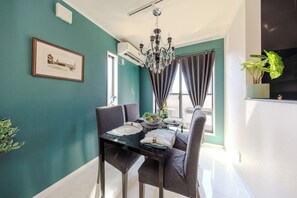Uma sala de jantar com uma mesa posta para quatro pessoas, um lustre e um quadro na parede.