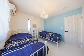 Quarto com duas camas, um candelabro, um guarda-roupa e uma pequena mesa.