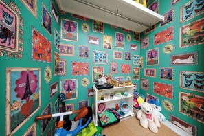 Quarto com paredes verde-água decorado com quadros, prateleira branca com brinquedos e um urso de pelúcia.