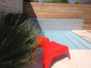 Une piscine avec une terrasse en bois et un fauteuil de relaxation rouge.