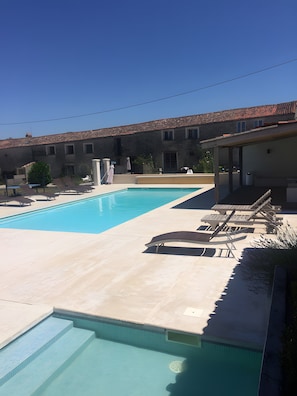 Piscina com espreguiçadeiras, área de estar coberta e edifício com telhado de azulejos.