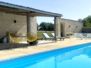 Ein Pool mit Liegestühlen, einer überdachten Lounge und Steinmauern.