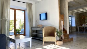 Amplia sala de estar con una mesa de comedor, una silla de mimbre, un televisor montado en la pared y una escalera que sube a otra habitación.