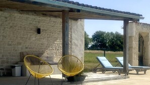 Zona junto a la piscina con un edificio de piedra, dos sillas amarillas y sillones de descanso.