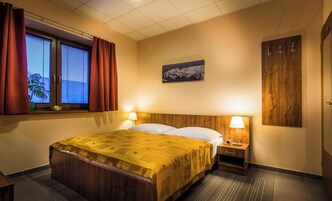 Una habitación de hotel con cama, lámparas de noche, ventana con cortinas, un cuadro colgado en la pared y un armario de madera.