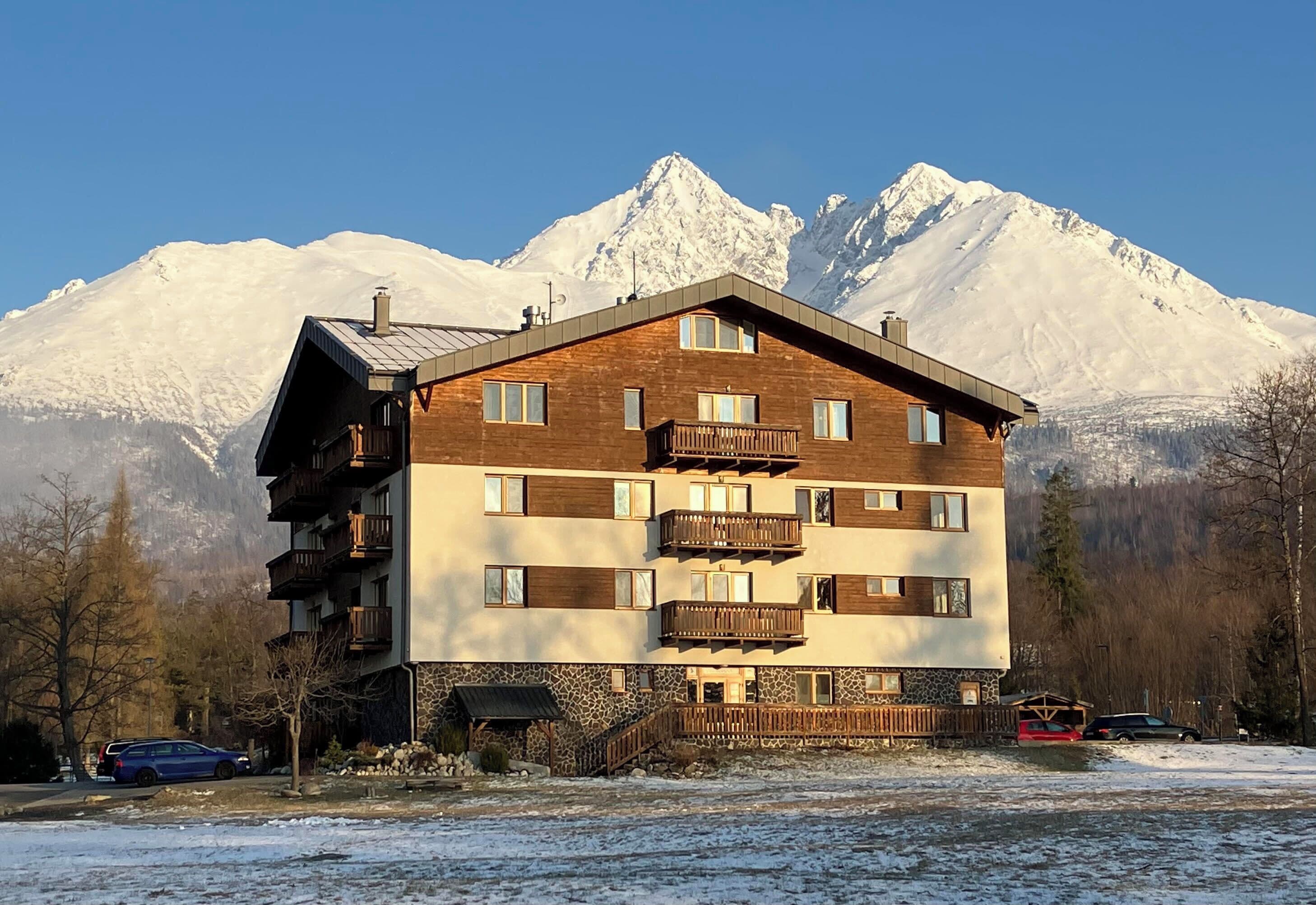 A multi-story building with balconies, a stone facade, and a view of snow-capped mountains.