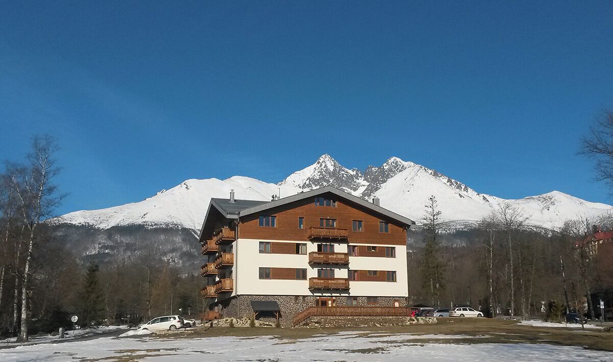 Un hotel de diverses plantes amb balcons, davant d'unes muntanyes cobertes de neu.
