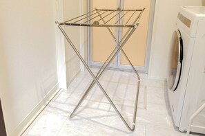 Uma área de lavanderia com um varal de metal, uma máquina de lavar e uma porta que dá para um cômodo.