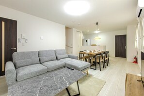 A modern living room with a grey sectional sofa, a marble coffee table, a dining area with a wooden table and chairs, and a kitchen in the background. - 8minute drive from Nagoya Station Brand new en / Nagoya City Aichi (Nagoya City)