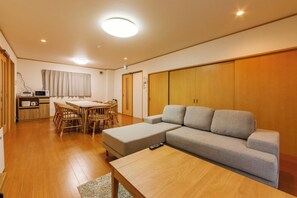 Ein modernes Wohnzimmer mit einer Couch, einem Esstisch mit Stühlen, einer Küchenzeile mit Mikrowelle und einem großen Kleiderschrank.